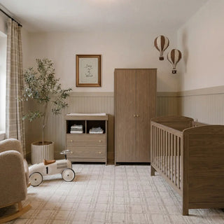 Nursery room with two cribs, a wooden dresser, a decorative tree, and hot air balloon wall decor.