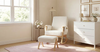 Rocking chair beside small table with a vase of flowers, white dresser, and pink rug on wooden floor in bright room.